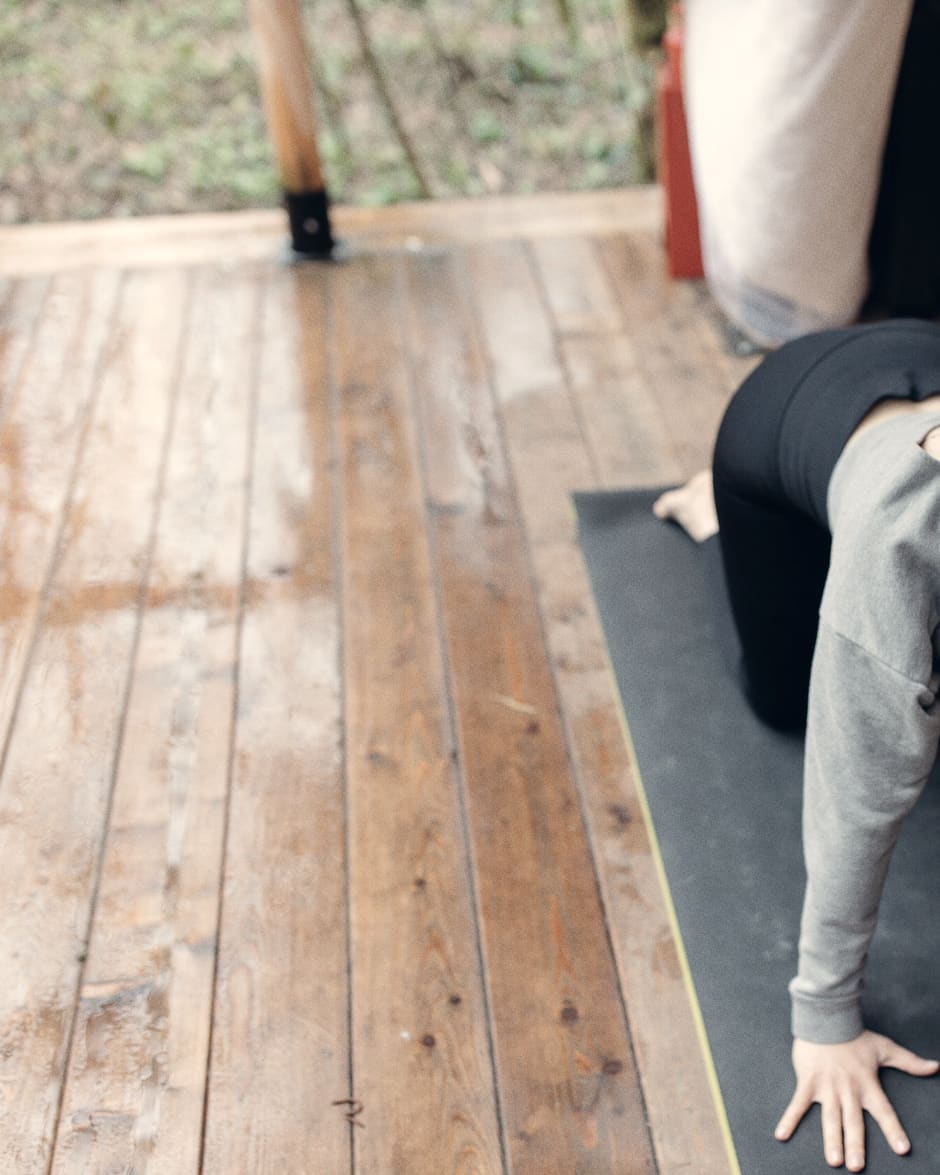 A practitioner low on the mat across wide warm floorboards, alone in a quiet room